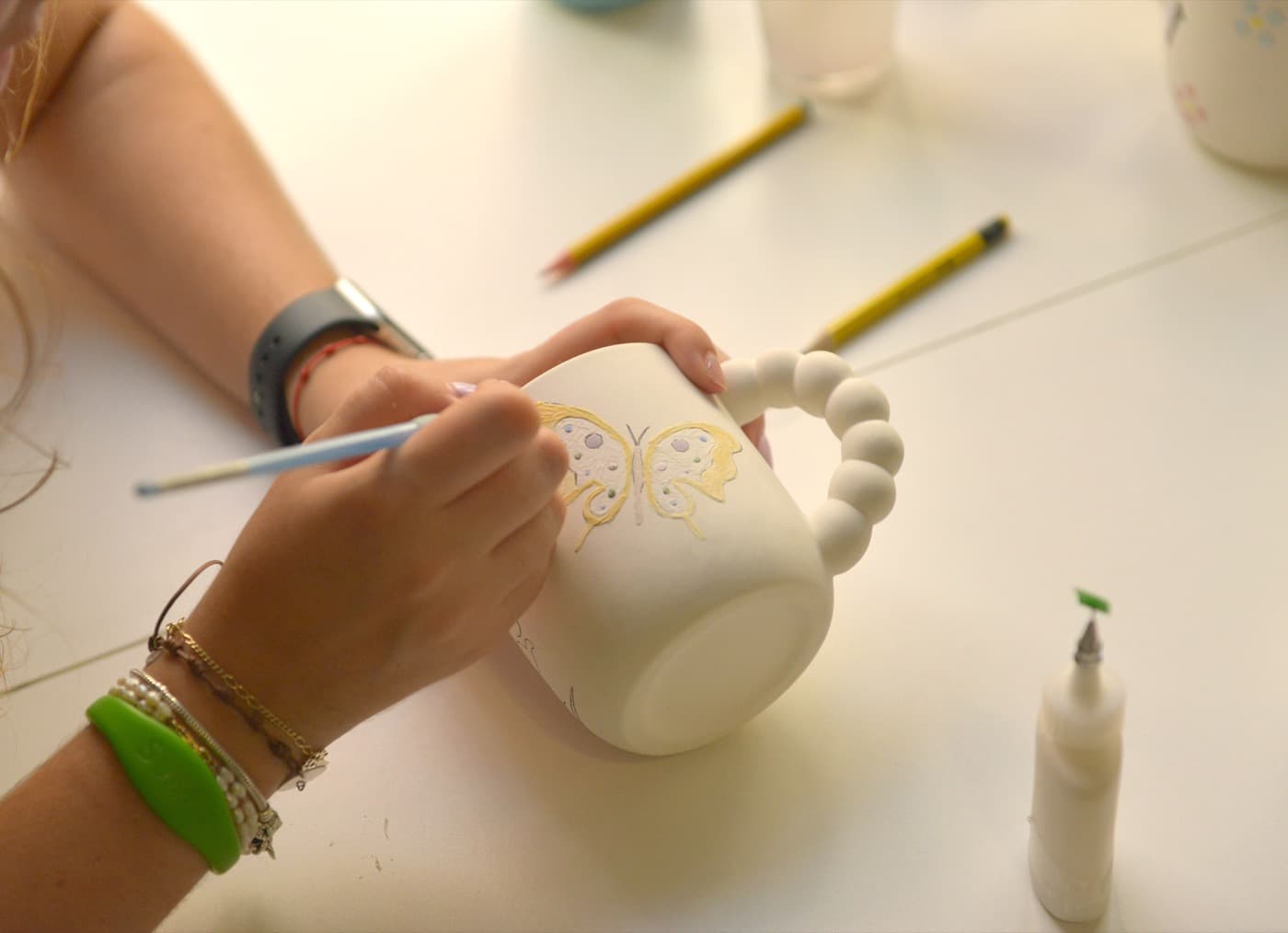 Persona joven pintando una mariposa en una taza de cerámica
